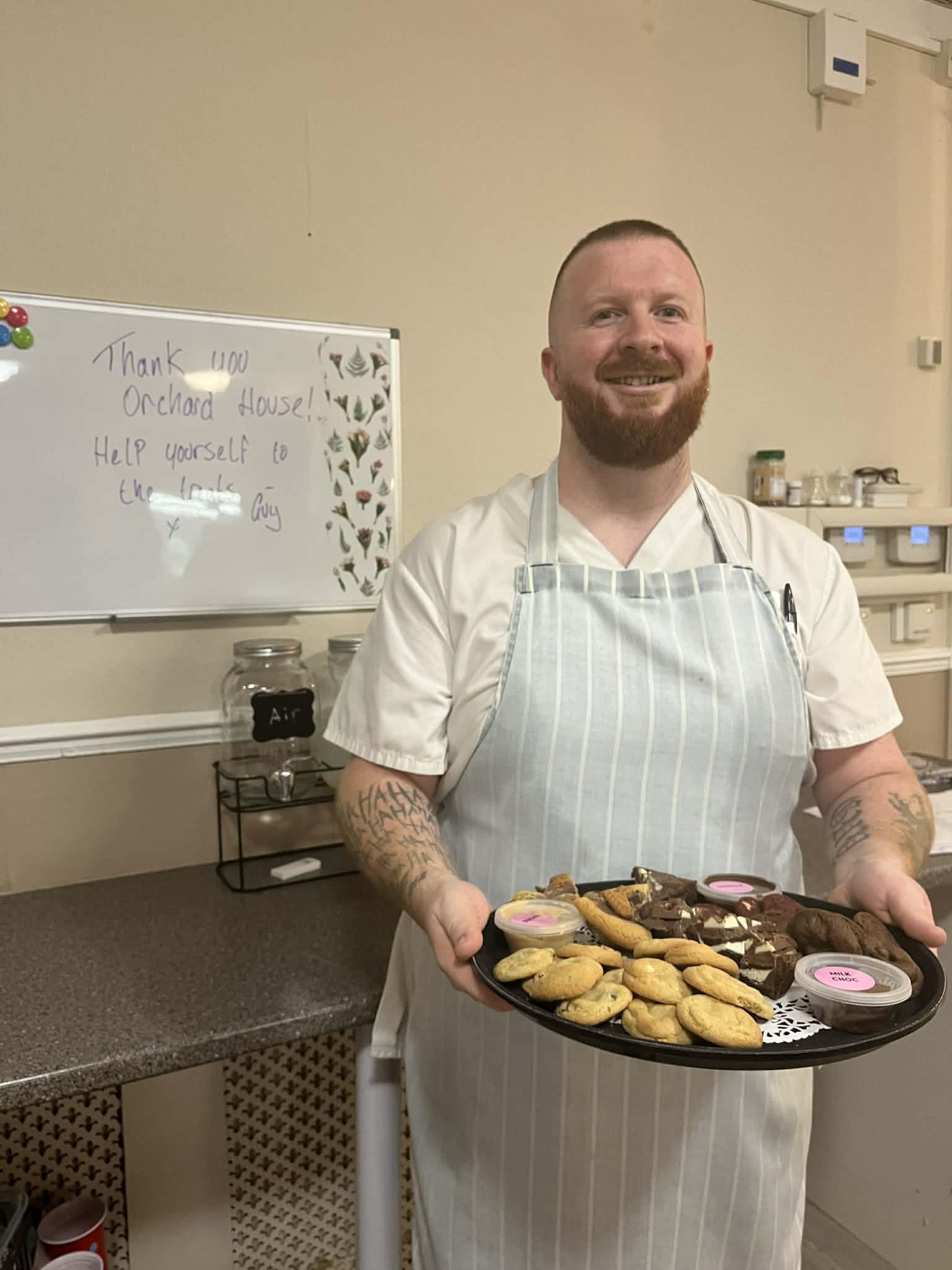 Staff member holding a tray of cookies and desserts in a care home kitchen.