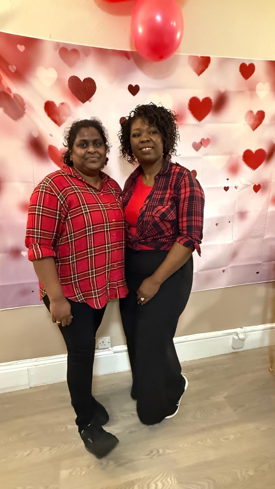 Two women smiling in front of Valentine’s themed backdrop