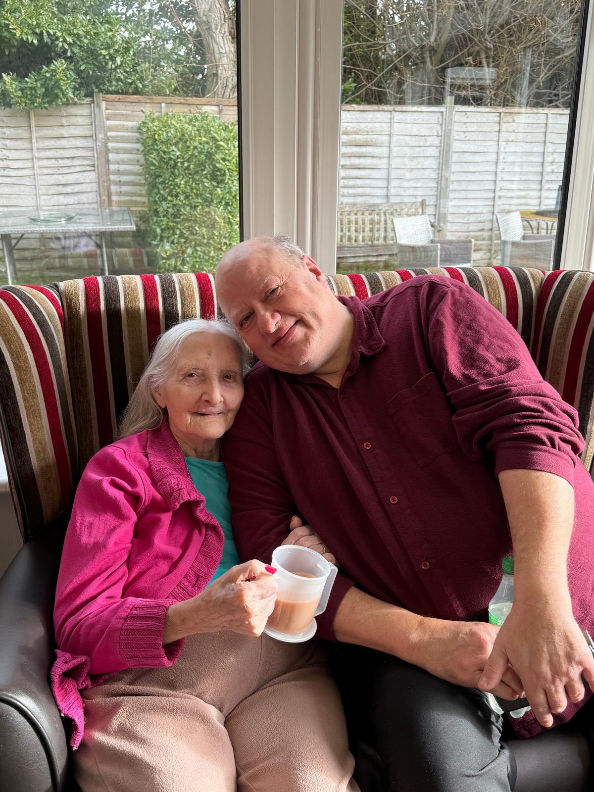 Elderly woman and man sitting together smiling with a cup of tea.