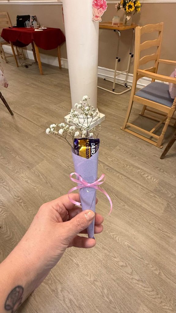 Hand holding a small gift with flowers and chocolate