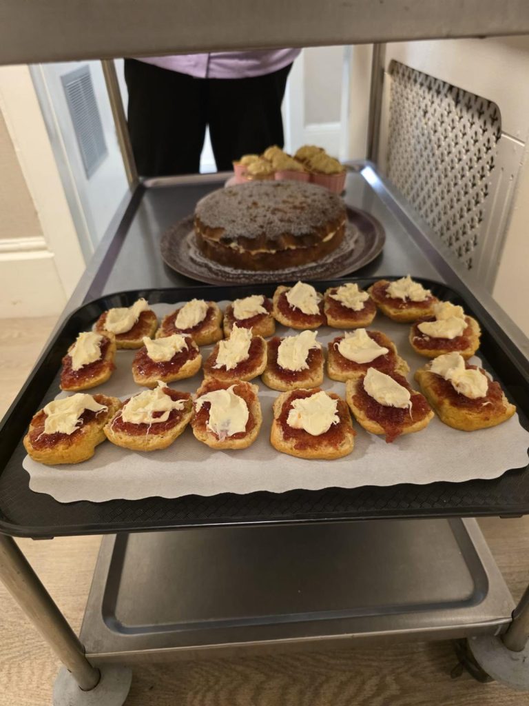 Tray of jam-and-cream scones with a cake on a trolley