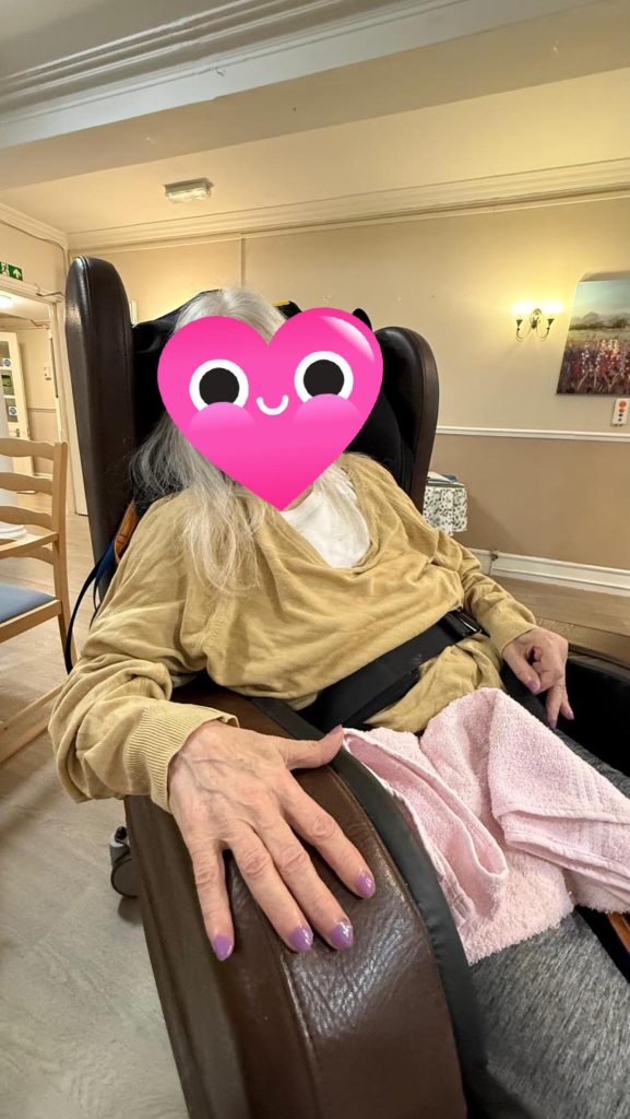 Elderly woman relaxing in a chair with freshly painted purple nails.