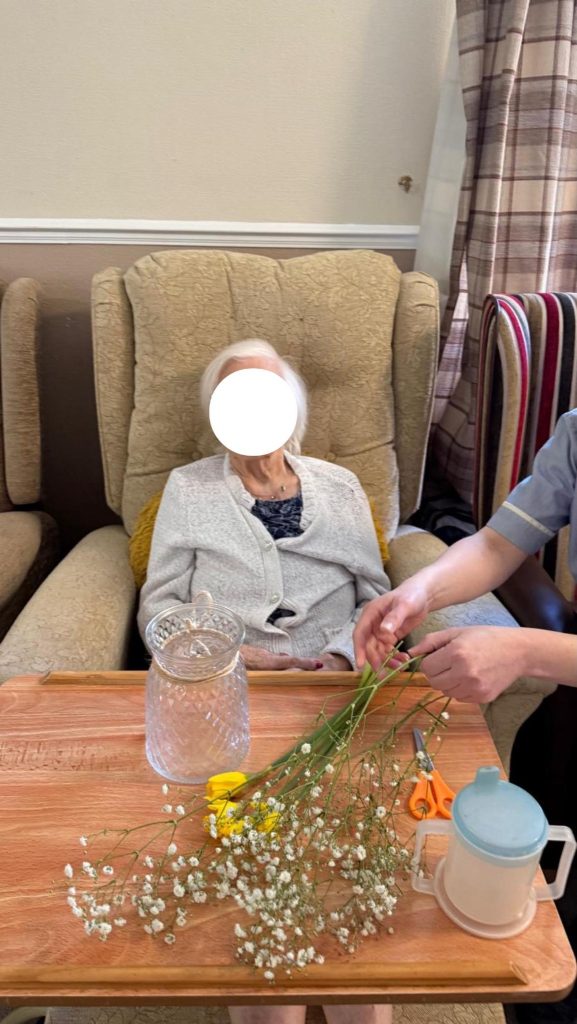 Elderly woman holding delicate white flowers while arranging a bouquet.