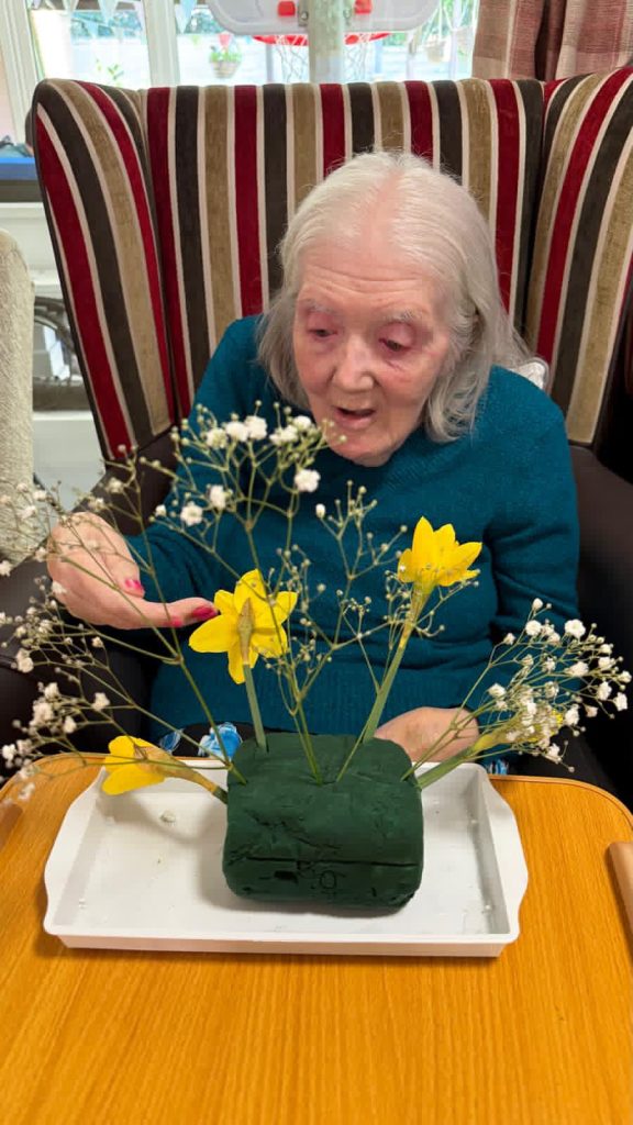 The same woman adding bright yellow daffodils to a delicate floral arrangement, focused on her work.
