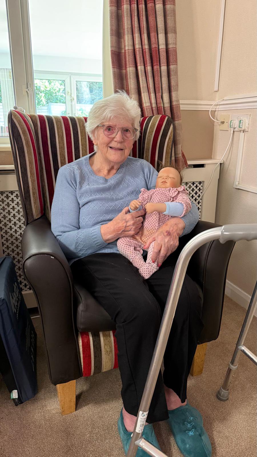 Elderly woman sitting in a chair holding a baby doll