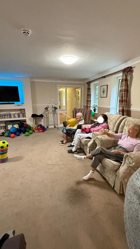 Elderly residents tossing a yellow ball toward a stacked ring target.
