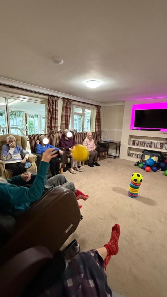 Resident throwing a yellow ball during a group game while others watch.