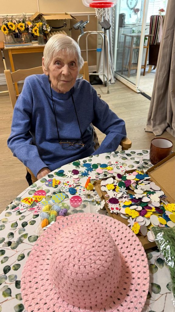 Elderly person at a table with Easter craft supplies, smiling gently.