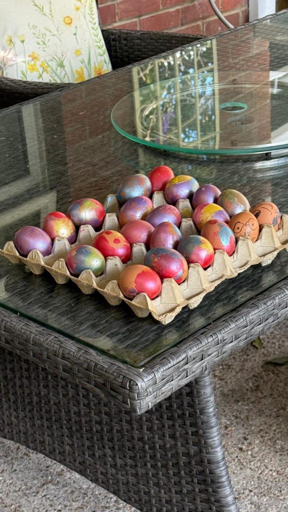 Tray of colorful painted eggs on a glass outdoor table.