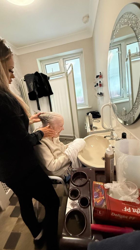 Care worker washing an elderly woman’s hair at a sink.