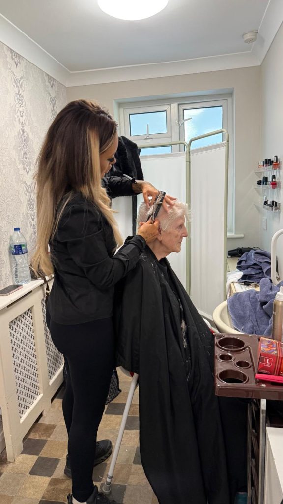Care worker cutting an elderly woman’s hair while she sits in a chair.