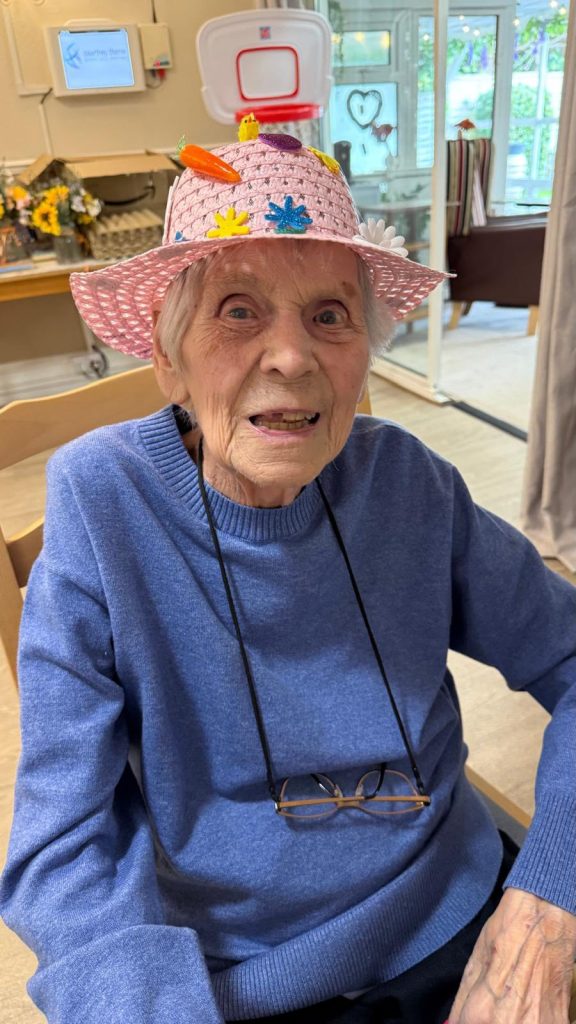 Elderly person smiling while wearing a decorated pink Easter hat.