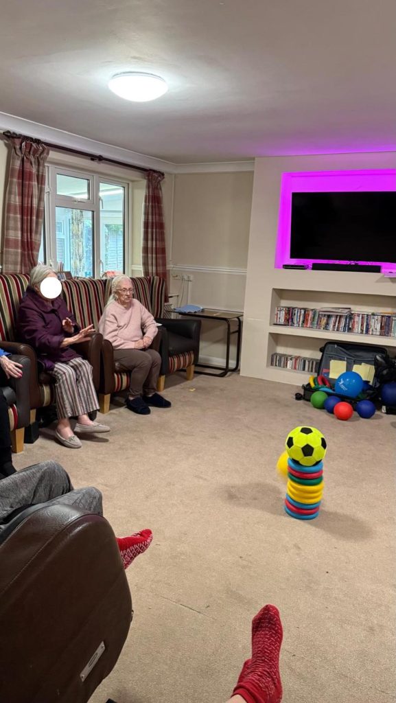 Residents participating in a group ball game with colorful equipment in a lounge.