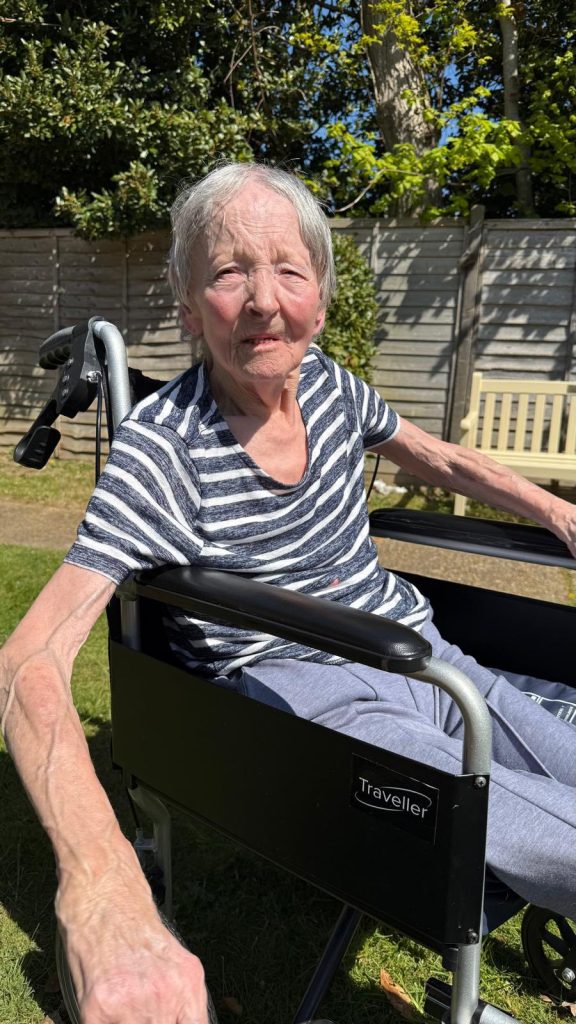 Close-up of an elderly woman sitting in a wheelchair outdoors in bright sunlight.

