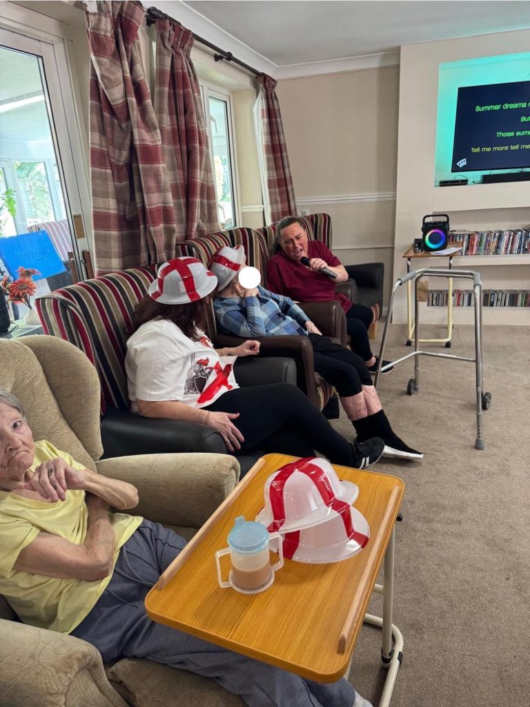 Residents in a lounge wearing England hats, singing karaoke together.