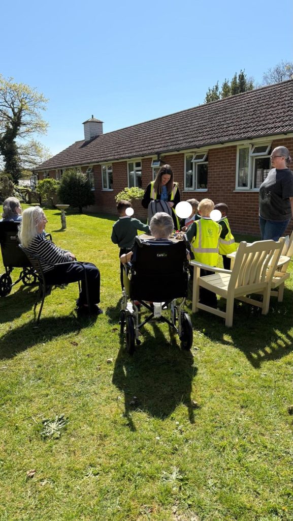 Care home residents watching children and staff during an outdoor activity on a lawn.