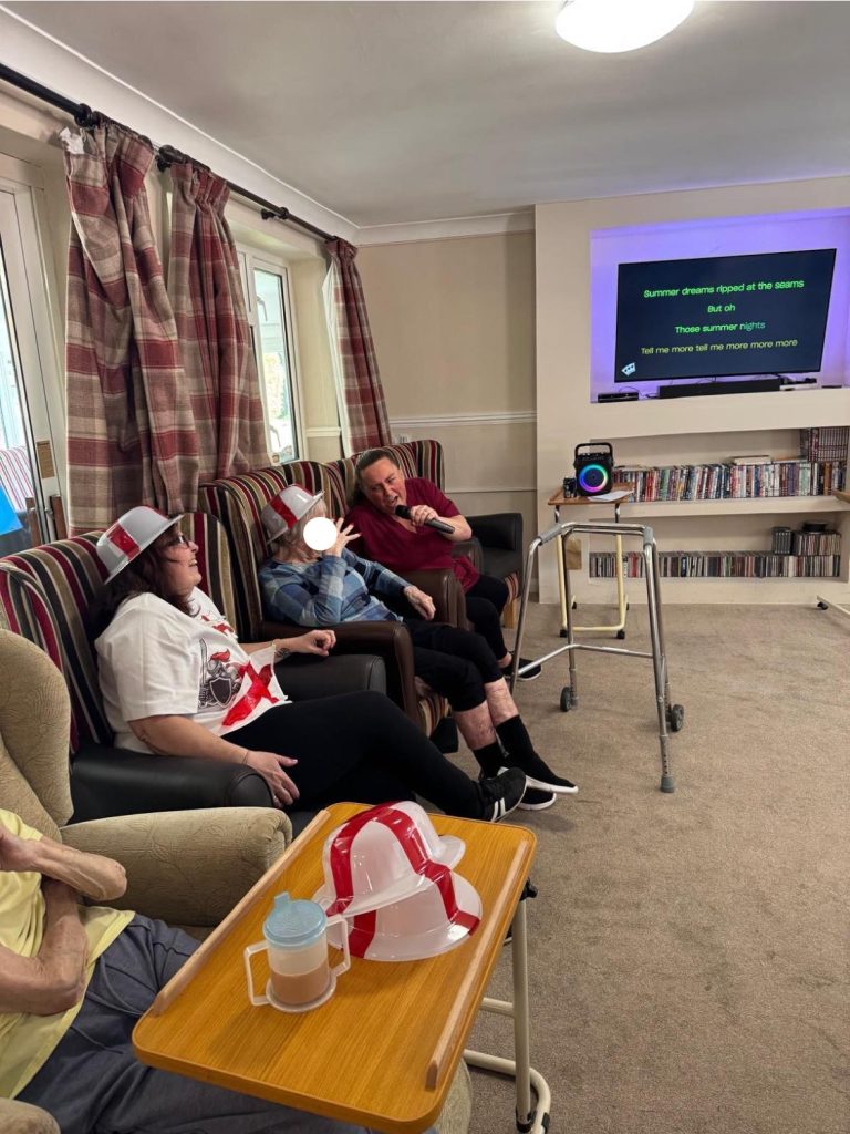 Group seated in armchairs watching and singing along to karaoke lyrics on TV.