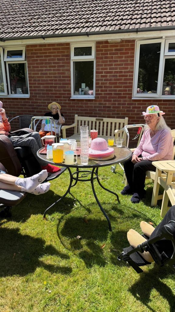 Group of elderly residents relaxing outdoors around a table with drinks on a sunny day.