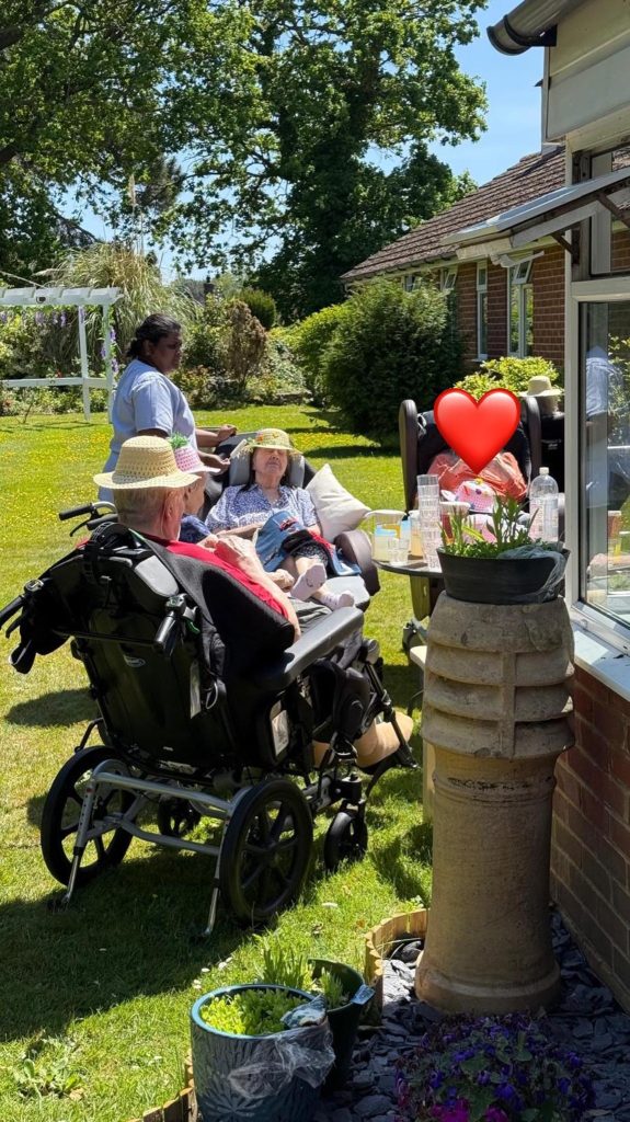 Residents relaxing outdoors in a care home garden on a bright summer day.