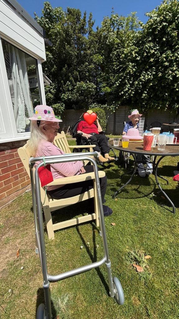 Elderly residents seated outside in the sunshine, socialising near a garden table.