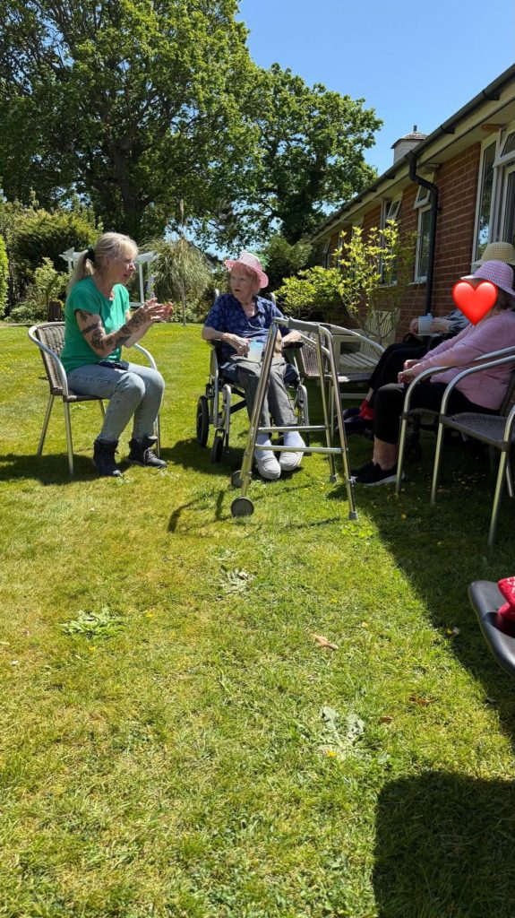Residents enjoying a sunny outdoor garden gathering, seated in a circle and chatting.