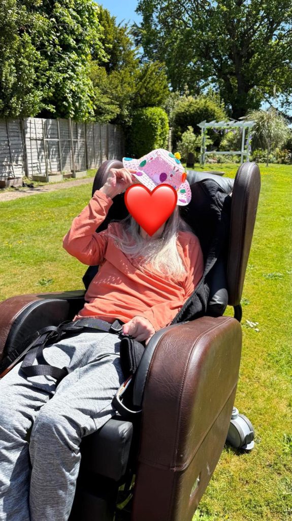 Older adult wearing a colorful hat while relaxing outdoors in a sunny garden.