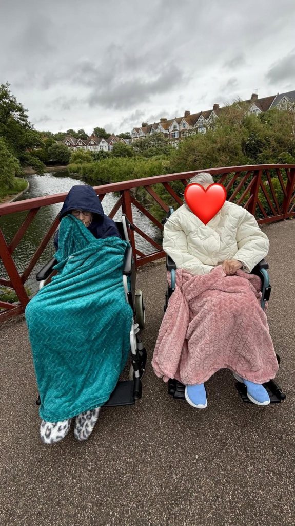 Two residents in wheelchairs enjoying a peaceful walk across a bridge by the water.