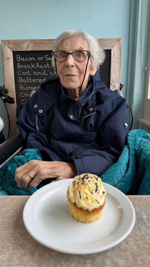 Resident smiling while enjoying a treat during a café visit by the sea.