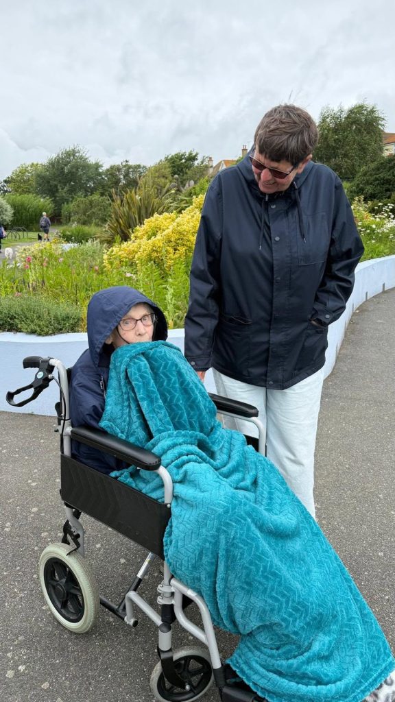 Resident enjoying a garden outing with a companion, wrapped warmly in a wheelchair.