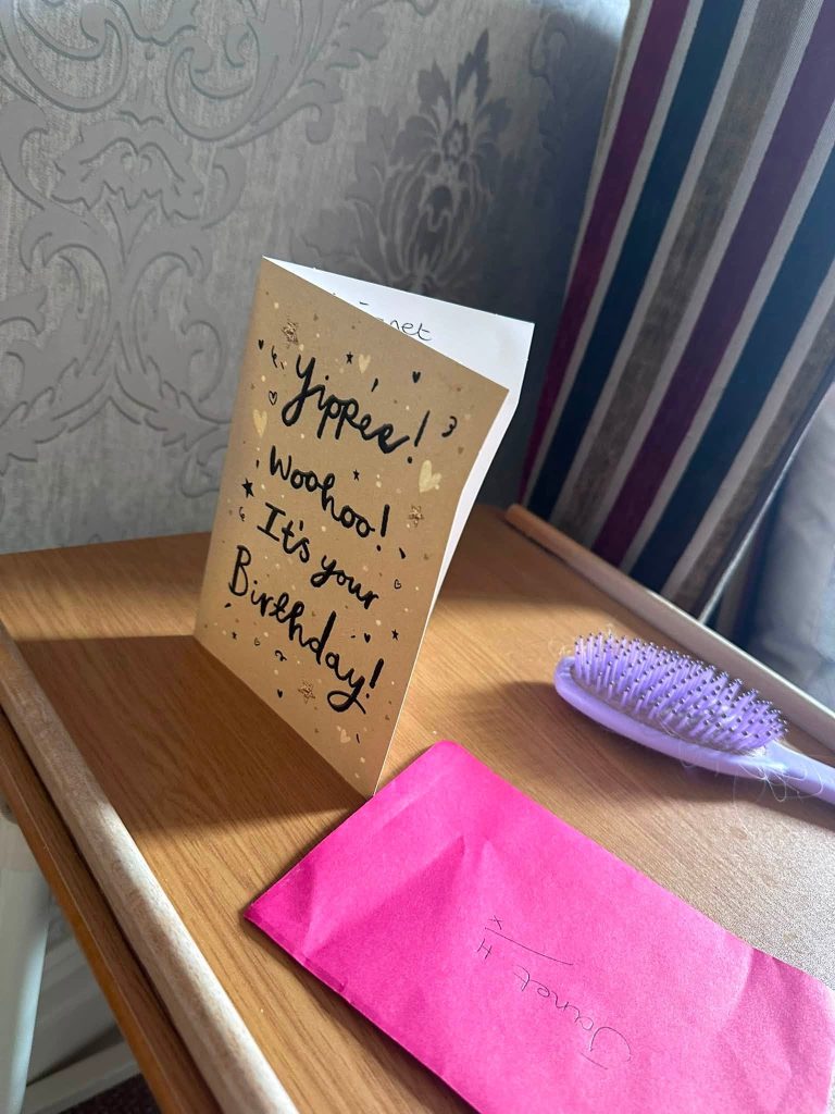 Birthday card and pink gift envelope displayed on a bedside table.