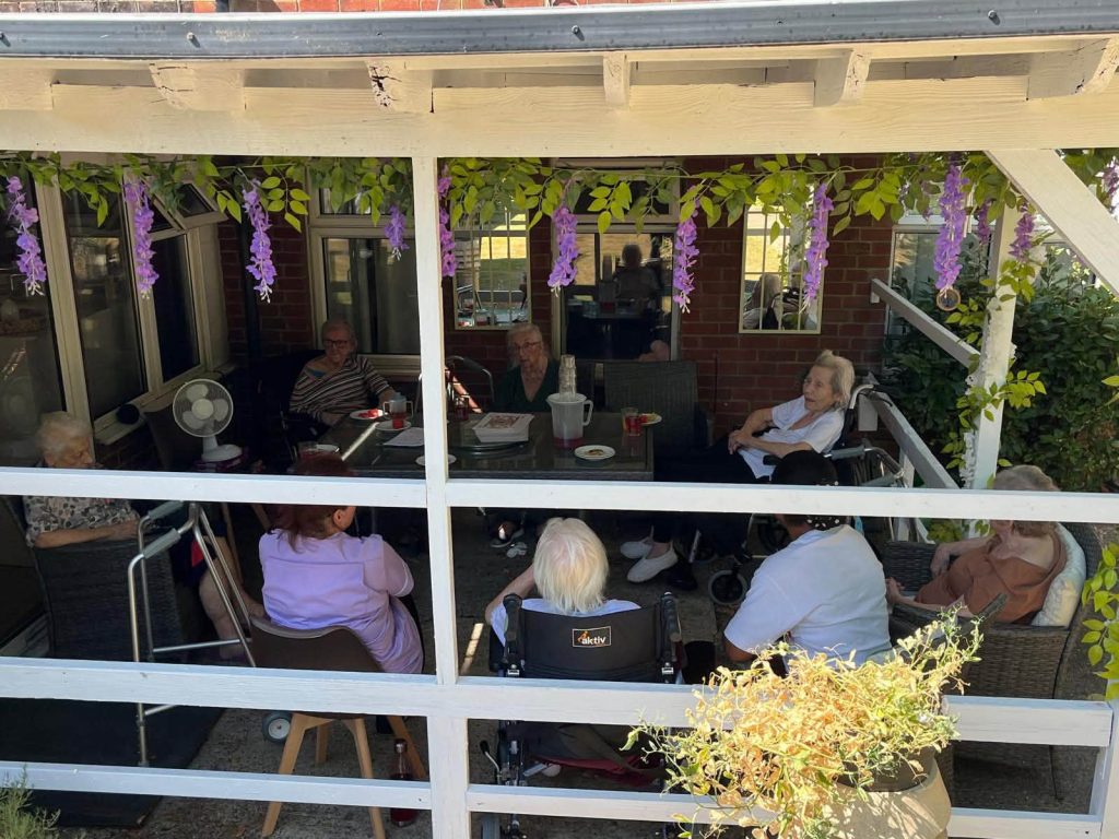 Group of elderly residents enjoying a social gathering on a covered outdoor patio.