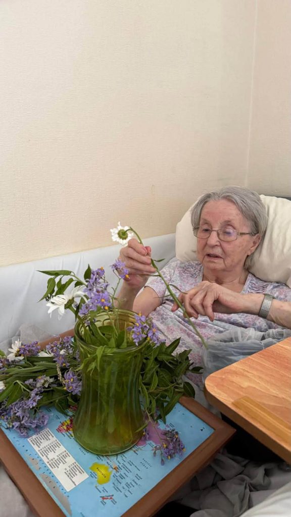 Elderly woman arranging fresh wildflowers in a vase while enjoying a relaxing bedside activity.