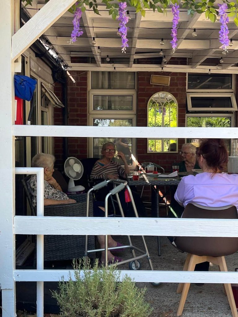 Residents and a care team member enjoying conversation together in the outdoor garden seating area at Orchard House Nursing Home.