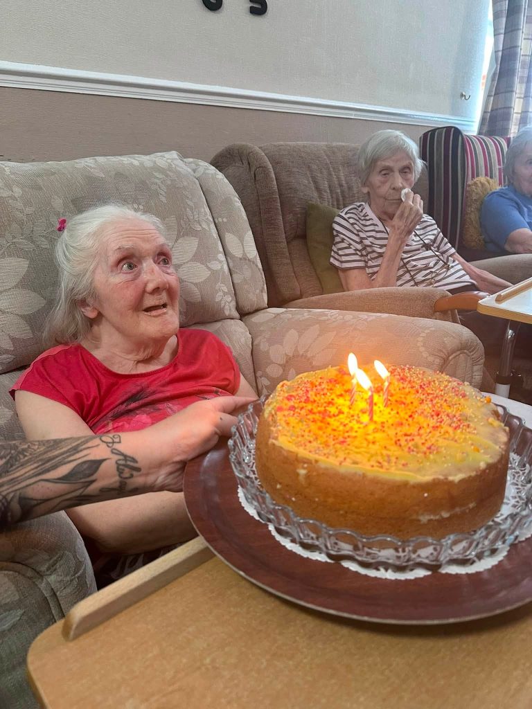 Smiling resident celebrating a birthday as a cake with lit candles is presented.