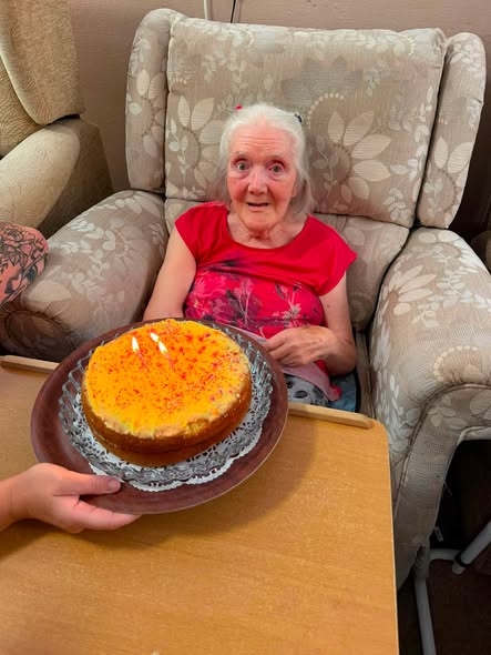 Resident smiling with surprise as a birthday cake with lit candles is brought over.