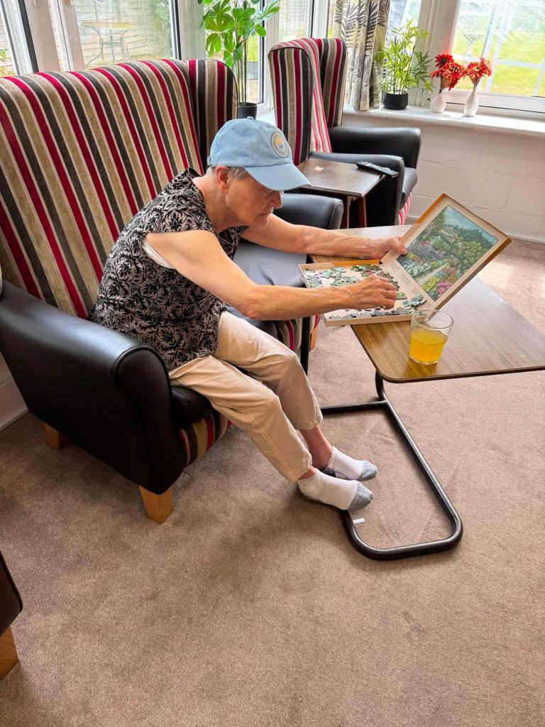 Resident enjoying a jigsaw puzzle in a comfortable lounge with a glass of juice nearby.