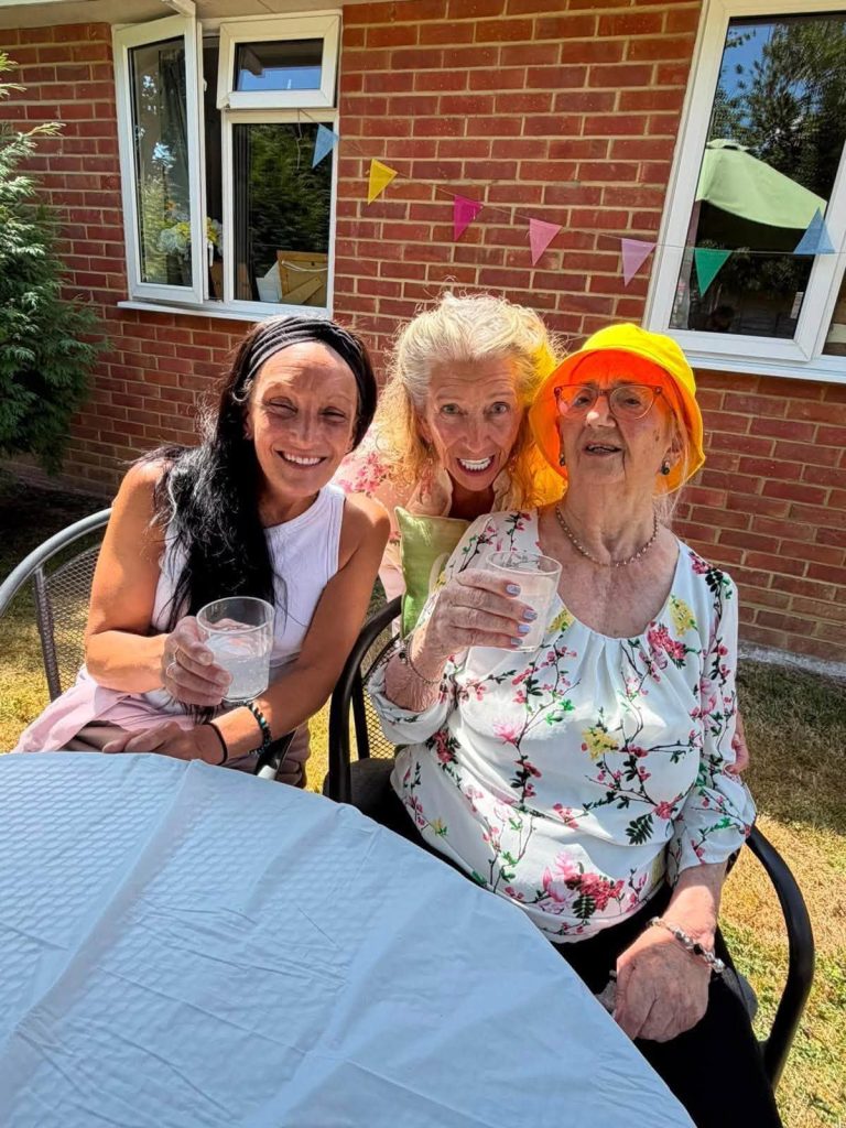 Resident smiling with family members while enjoying drinks outdoors.