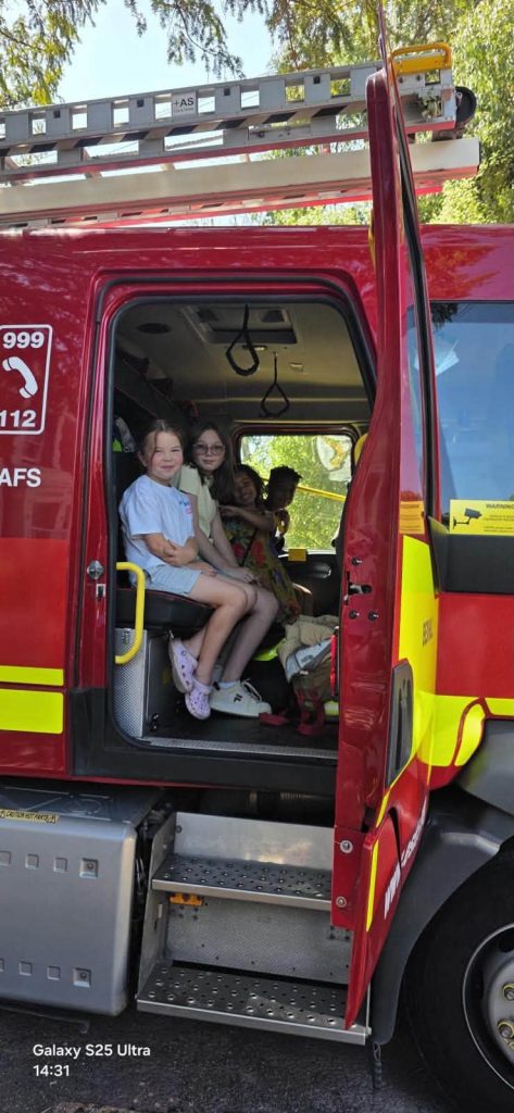 Children smiling inside a fire engine during a fire station visit.