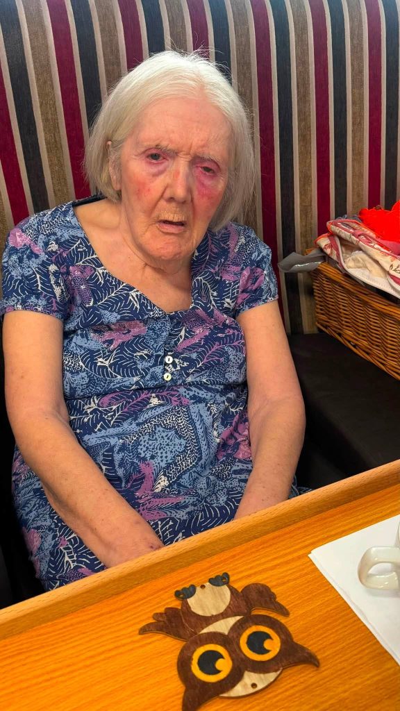 Elderly woman sitting at a table with an owl craft.
