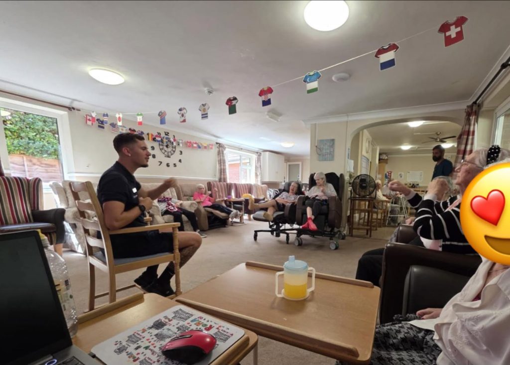 Group of older adults take part in a lively seated activity.