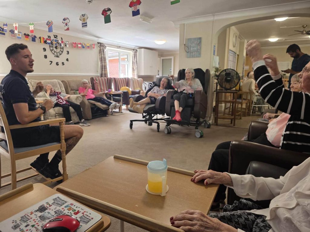 Resident reaches for a yellow ball during a seated activity.