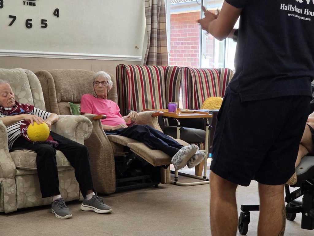 Older adults participate in a seated ball activity with a caregiver.