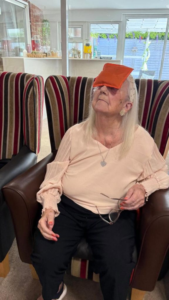 Older woman holding a blue beanbag over her face during an activity.