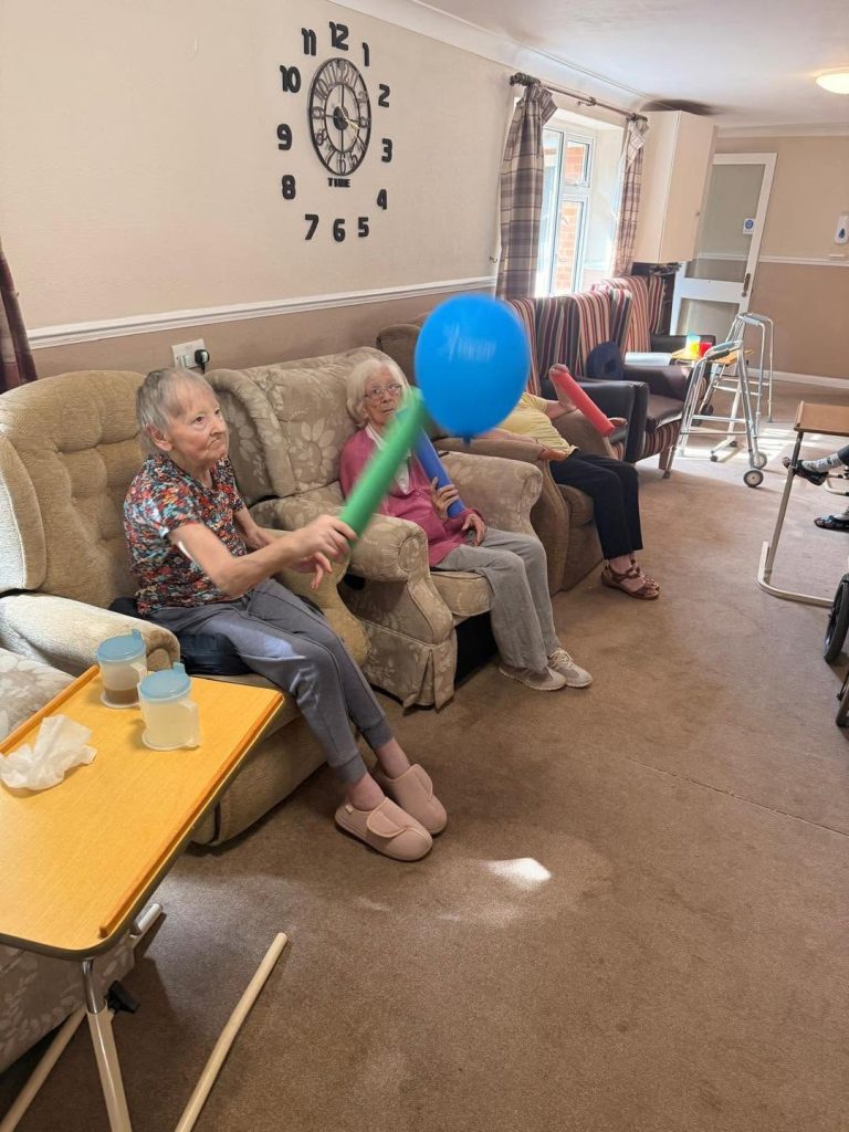 Older residents playing a seated ball game with colorful equipment.