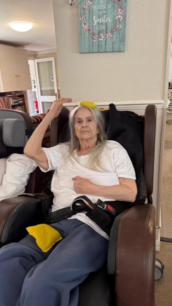 Elderly woman seated in a chair with a yellow beanbag on her head.