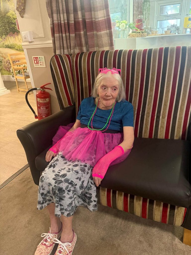 Elderly resident dressed in a pink tutu and accessories for an 1980s-themed care home celebration.
