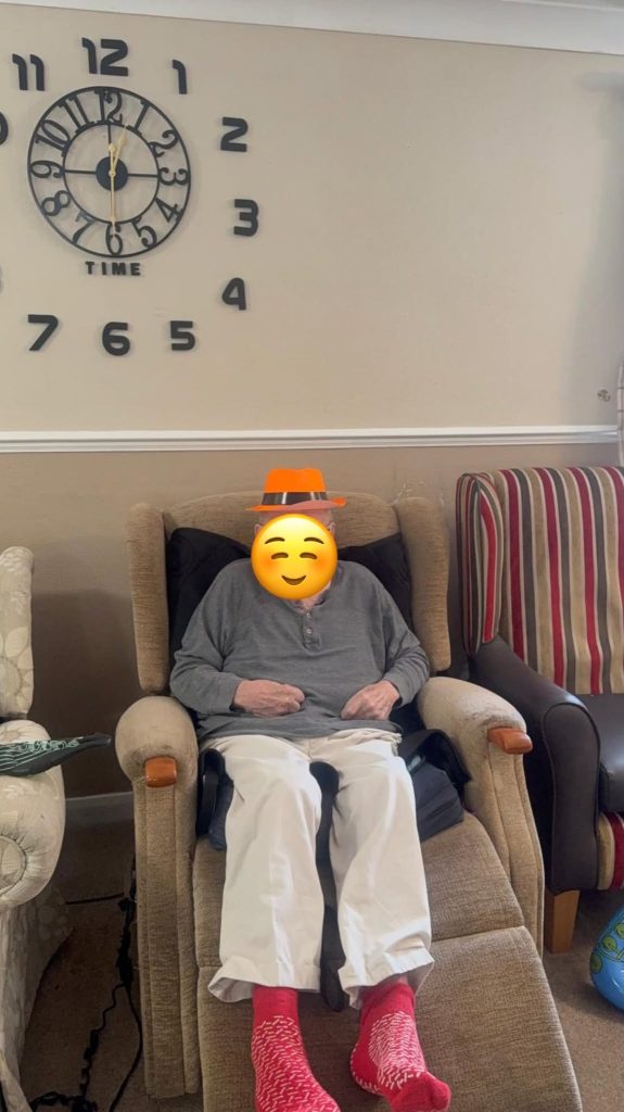 Elderly resident relaxing in a comfortable armchair wearing a festive hat and red socks.
